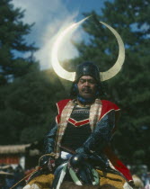 Man on horseback in a Samuri Costume with the sun reflecting off his horned helmet