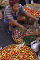 Fruit and vegetable vendor crouching by baskets of goods with customer at Carbon Market