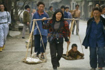 Woman with carrying scales over her shoulders balancing a small child with a sack.