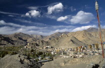 Prayer flags hanging above village set in mountainous landscape with hilltop palace in the distance