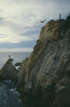 Cliff diver in mid air with sea below