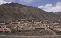 View over Labrang Monastery surrounded by hills and people walking a path in the foreground