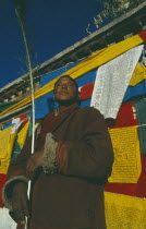 Male pilgrim standing outside temple in front of prayer flags