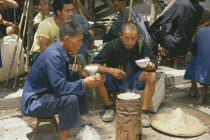 Two elderly men cooking meal at roadside stall.