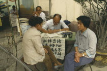 Professional letter writer with customers sitting at a desk outside the post office