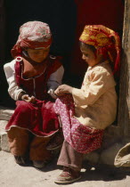 Two Tadjik girls sitting on step beside wooden door frame.