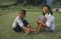 Two farm girls sitting on grass laughing.