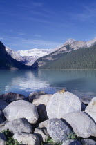 View over boulders and clear blue water toward snow covered rocky mountains with a chipmunk sitting in the foreground