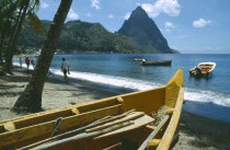 People walking past fishing boats on beach with the Pitons in the distance