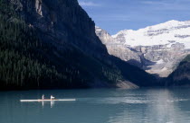 Canoeist on Lake Louise with a backdrop of snow covered sheer cliffs and pine forests