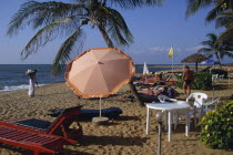 Sandy beach with umbrella shading tourists lying on sunbeds and a shell vendor dressed in white