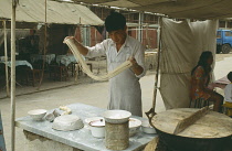 Young man making noodles at food stall by swinging the dough into thin strips.