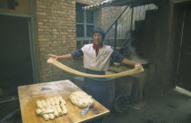 Smiling young man making noodles  holding long ribbons of dough in outstretched arms.