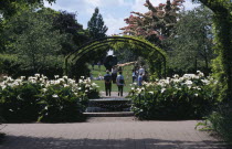 Wisley Royal Horticultural Society Garden. Visitors walking along pathway through arch towards Henry Moore sculpture.European Great Britain Northern Europe UK United Kingdom British Isles Order Fello...