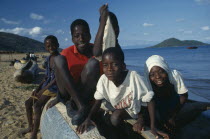 Group of children sitting on boat on lake shore.