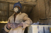 Dedza Potteries producing Fair Trade goods for export.  Craftsman wearing protective mask and overalls to grind rock.