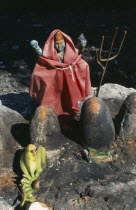 Decorated figure in Hindu shrine with offerings of fruit and flowers.