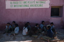Sahrawi schoolgirls sitting against pink plastered wall under banner with slogan in French: RASD is a national and international irreversible reality.SADR Sahrawi Arab Democratic Republic Morocco dis...