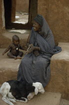 Portrait of woman sitting beside young child with sheep at her feet.West Africa