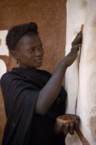 Young woman decorating exterior wall of mud building with ochre.  It is traditional for women to both design and apply such decorations.West Africa