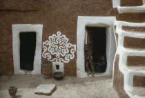 Mauritania, Qualata, Traditional mud architecture decorated with bas relief motif of applied gypsum, white and red clay, with children framed in open doorway.