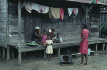 Local family sitting on raised wooden veranda of their home with line of washing hanging overhead.