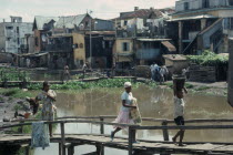 Children crossing wooden bridge over stagnant water in poor housing area near Antananarivo.Tana
