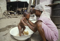 Young mother washing baby in bowl in street.cleanhygiene