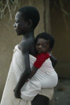 Child carrying sibling on her back wrapped in white cotton cloth.