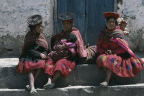 Women carrying children in blanket slings resting in plaza after walk from village.Ollantaitambo Cusco