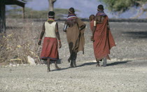 El Molo tribeswomen wearing traditional jewellery with one carrying child in sling on her hip  all walking away from camera.