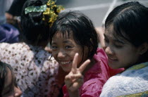 Young girl smiling and making the V peace sign with fingers amongst other girls at water festival