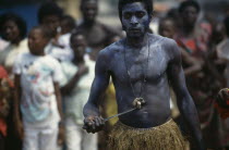 Man holding knife to his stomach during juju ceremony to summon ancestor spirits.