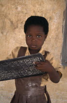 Portrait of pupil from primary school in village near Accra holding small blackboard printed with alphabet and numbers.
