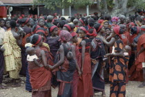 Group of women carrying babies on their backs at Ashanti funeral  dressed in red the colour of mourning.  Large mixed crowd in background.Asante Color