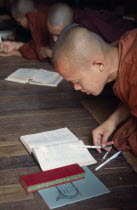 Monk at wooden desk with books in Ywama MonastryBurma Myanmar