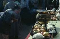 Woman praying at an open air altar. Insense burning in a gold urn on table with offerings of fruit and rice bought their by people for Buddhas Birthday