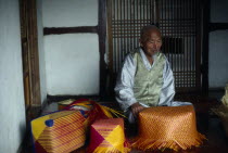 Portrait of Kim Tong Yon a master bamboo craftsman who has been declared a Living National Treasure by the government. Seated indoor with examples of his colourful  baskets