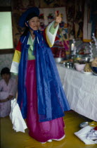 Female Shaman with arm raised in air at a funeral wearing colourful clothing.Mudang whose role it is to act as a intermediary between the living and spirit worlds