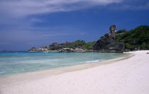 View along the sandy beach with people and boats near the rocky coast line.