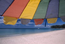 Close up of a multi coloured parasol on the sandy beach  boat in the distance. Colored umbrella