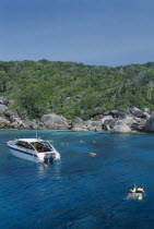 Snorkelers in the water next to a small motor boat near the rocky shore.
