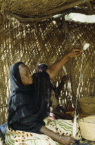 Woman spinning cotton inside straw hut