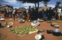 People at market selling fruit and vegtables on the ground with silver containers