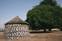 Traditional mud architecture.  Circular hut or granary with straw roof and black and white abstract pattern painted on wall.West Africa