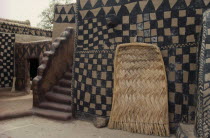 Traditional mud architecture.  Steps to flat roof where crops are dried and woven straw door.  Walls painted with black and natural chequered design.Sirigu village.  West Africa