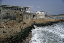 Cape Coast Castle.  Line of cannons along seventeenth century castle ramparts with children playing on rocks below.West Africa
