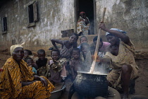 Woman in village near Accra stirring cauldron of fufu made from boiled and pounded cassava tubers surrounded by children and other women.foufou  eba  West Africa