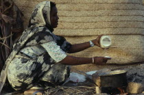 Beja nomad woman cooking mededa gruel made from sorghum over open fire.