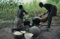 Dinka women cooking millet and sorghum in pots over open fire.